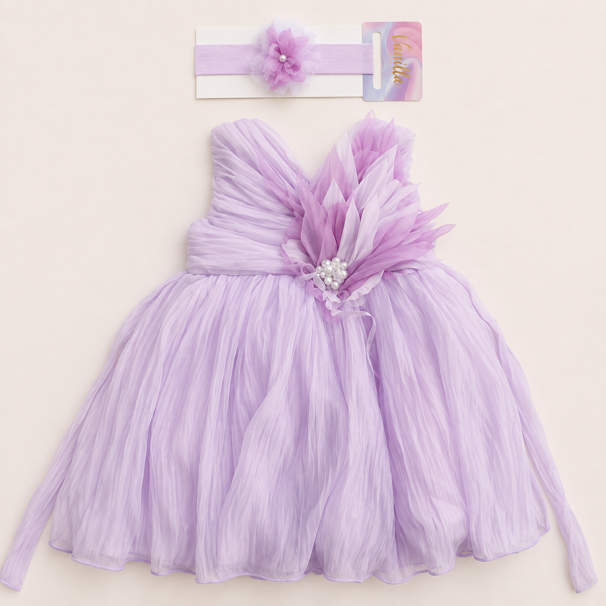 purple girls’ party dress with matching floral headband, featuring a pleated full skirt, layered fabric flower embellishment, pearl detailing, and delicate ribbon accents on a light background.