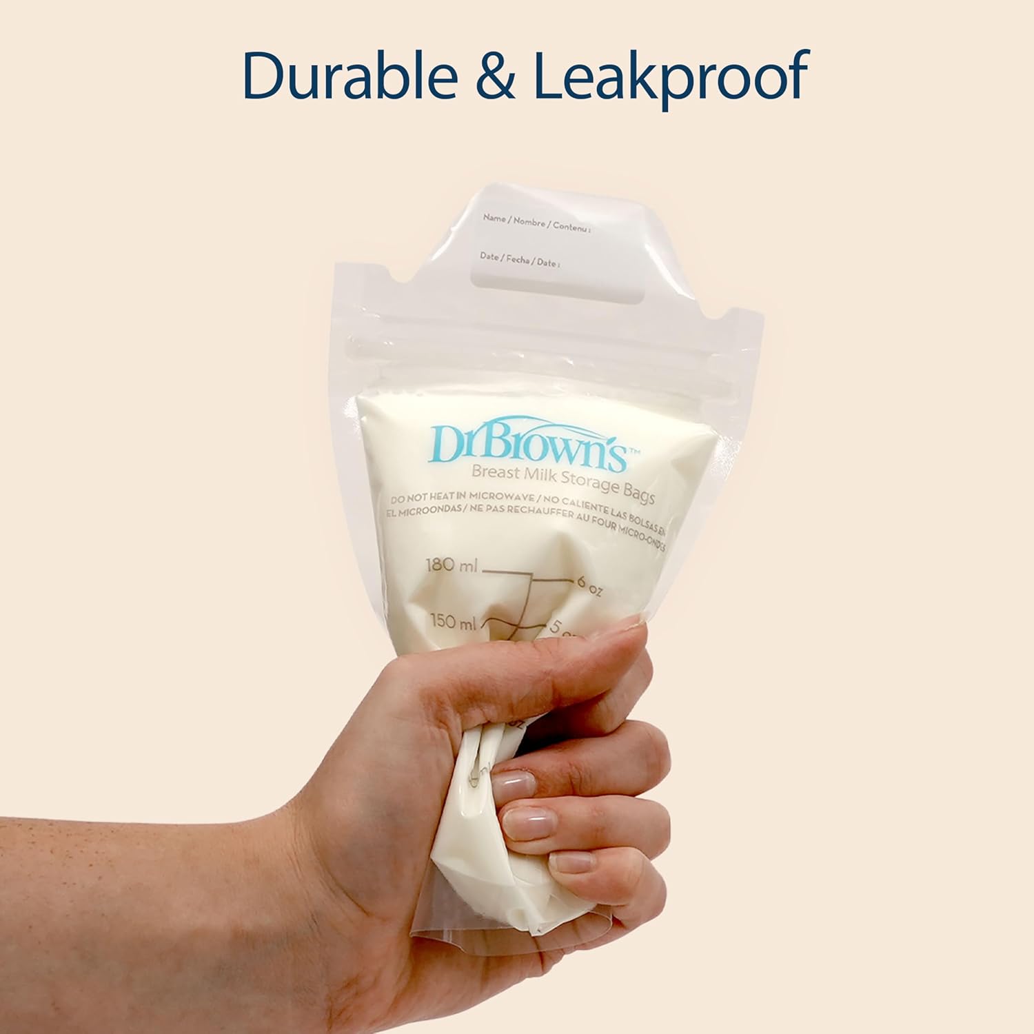 Hand holding a Dr. Brown's breast milk storage bag with 'Durable & Leakproof' text on a beige background